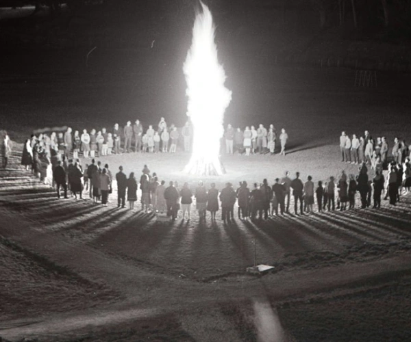 Um ein großes Feuer haben sich, in einem Kreis, viele Menschen versammelt.