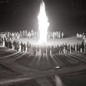 Um ein großes Feuer haben sich, in einem Kreis, viele Menschen versammelt.