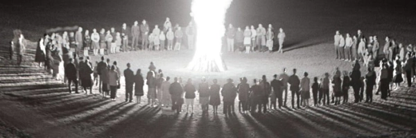 Um ein großes Feuer haben sich, in einem Kreis, viele Menschen versammelt.