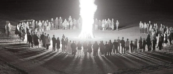 Um ein großes Feuer haben sich, in einem Kreis, viele Menschen versammelt.