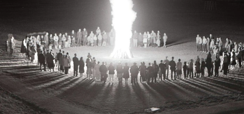 Um ein großes Feuer haben sich, in einem Kreis, viele Menschen versammelt.