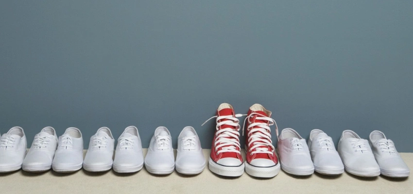 Ein Paar roter Schuhe steht in einer Reihe weißer Schuhe.