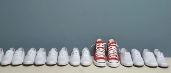 Ein Paar roter Schuhe steht in einer Reihe weißer Schuhe.