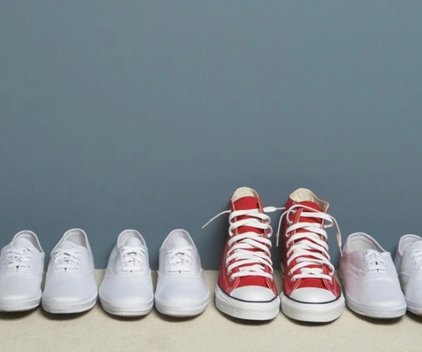Ein Paar roter Schuhe steht in einer Reihe weißer Schuhe.