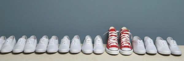 Ein Paar roter Schuhe steht in einer Reihe weißer Schuhe.