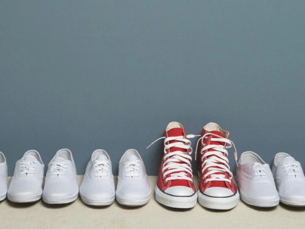Ein Paar roter Schuhe steht in einer Reihe weißer Schuhe.