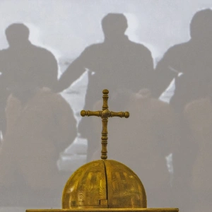 Ein Kreuz auf einer Kuppel. Im Hintergrund ist eine Christenverfolgung dargestellt.