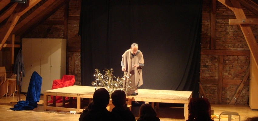 Ein Mann steht alleine auf einer Bühne und spielt eine Szene.