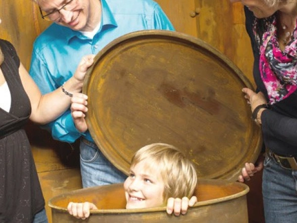 Einige Erwachsene stehen um eine Tonne, aus der, grinsend, ein Kind schaut.