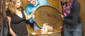 Einige Erwachsene stehen um eine Tonne, aus der, grinsend, ein Kind schaut.