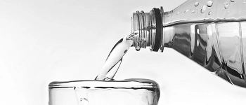 Wasser fließt aus einer Flasche in ein bereits überlaufendes Glas.