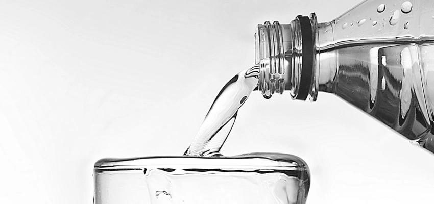 Wasser fließt aus einer Flasche in ein bereits überlaufendes Glas.