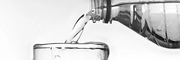 Wasser fließt aus einer Flasche in ein bereits überlaufendes Glas.
