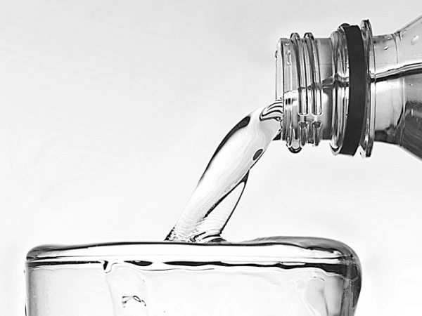 Wasser fließt aus einer Flasche in ein bereits überlaufendes Glas.