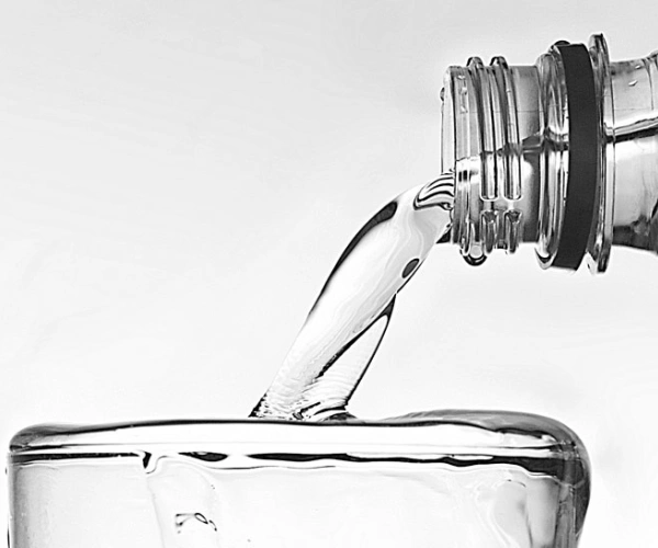 Wasser fließt aus einer Flasche in ein bereits überlaufendes Glas.
