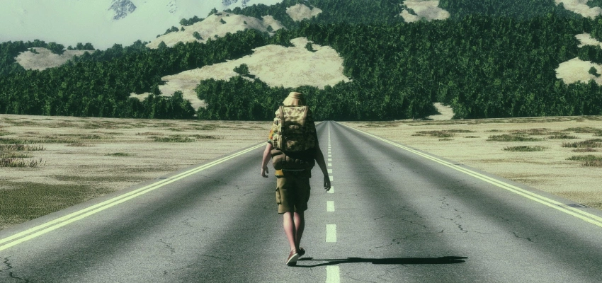 All-In-Man. Aufs Ganze gehen ohne dabei draufzugehen. Zu sehen ist ein Mann in Wanderklamotten auf der Straße Richtung den Bergen.