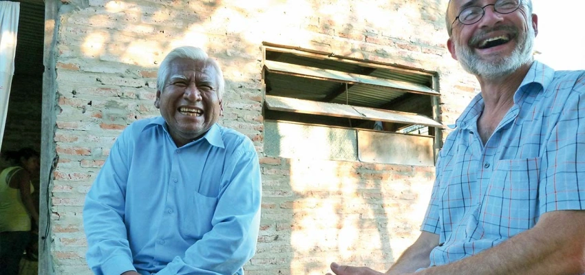 Zwei sitzende Männer lachen gemeinsam neben einem Haus in Argentinien