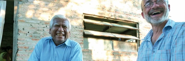 Zwei sitzende Männer lachen gemeinsam neben einem Haus in Argentinien