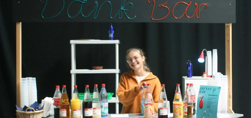 Lächelnde, in die Kamera guckende Frau steht hinter einer Getränkebar namens 