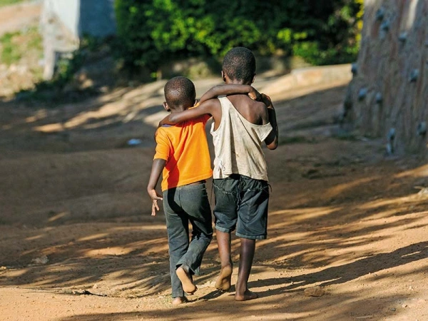 Zwei schwarze, barfüßig gehende, Kinder, Schulter an Schulter auf einem Sandweg