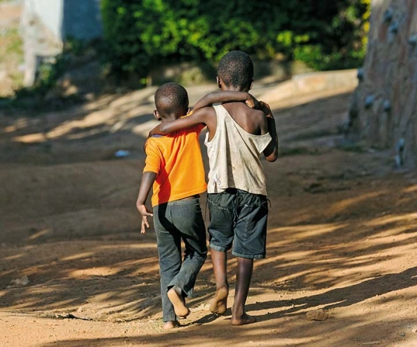 Zwei schwarze, barfüßig gehende, Kinder, Schulter an Schulter auf einem Sandweg