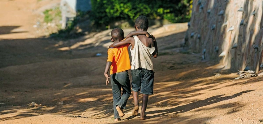 Zwei schwarze, barfüßig gehende, Kinder, Schulter an Schulter auf einem Sandweg