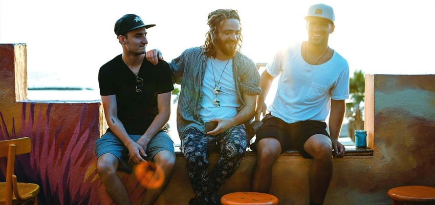 Drei lachende Männer sitzen auf einer Mauer mit der Sonne im Hintergrund