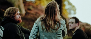 Zwei Männer und eine Frau sitzen auf einem Baumstamm