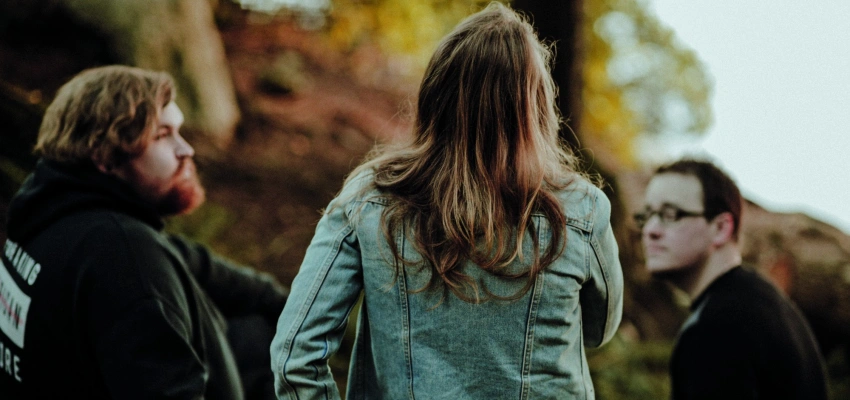 Zwei Männer und eine Frau sitzen auf einem Baumstamm
