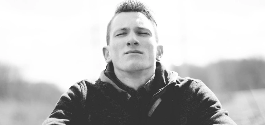 Junger Mann sitzt mit geschlossenen Augen, er scheint konzentriert zu sein.