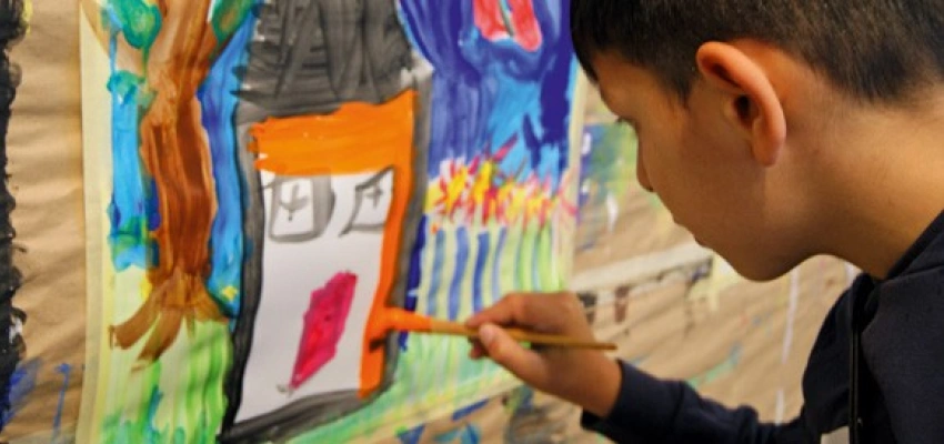 Junge bemalt ein Plakat mit einem bunten Haus inklusive Garten