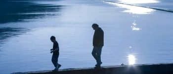 Zimzum – Zwei Menschen auf einer niedrigen Mauer umgeben von Wasser
