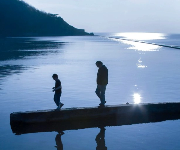 Zimzum – Zwei Menschen auf einer niedrigen Mauer umgeben von Wasser